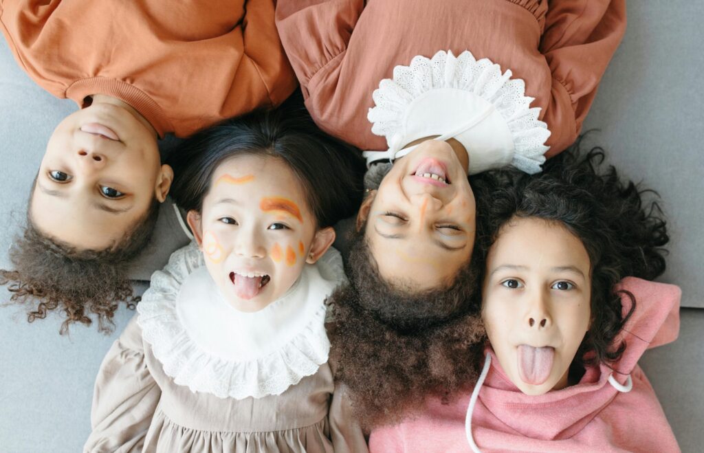 Four diverse children playfully posing on a gray sofa, expressing joy.